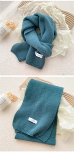 Detailed teal knitted scarf with thick rib edges and a white brand label for winter warmth