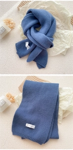 Detailed texture of thick blue knit scarf with ribbed edges and minimalist brand label