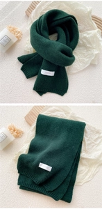 Detail shot of chunky knit dark green scarf with brand label and wool texture