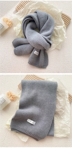 Detailed close-up of grey knitted scarf texture with brand label on minimalist background