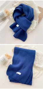 Detailed texture of thick navy blue knit scarf with ribbed edges and minimalist white tag