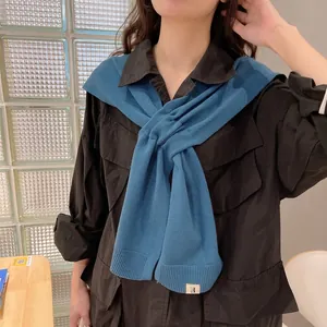 Chic blue knitted shawl wrap with decorative tag worn over a black shirt for styling
