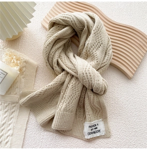 Detail of warm beige knit scarf with delicate texture and woven label on wooden board