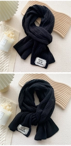 Close-up of black cable knit scarf texture featuring a minimalist white woven label