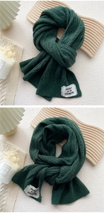 Detail showing deep green chunky knit texture and woven logo patch on warm scarf