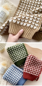 Detail of knitted winter scarf with white heart patterns in various warm color tones
