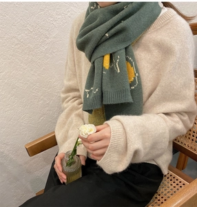 Macro detail of dark green knit scarf with yellow geometric patterns and soft texture