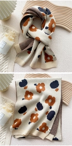 Detail of a thick knitted scarf featuring blue, orange, and cream floral patterns