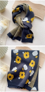 Detail of knitted scarf showing yellow sunflower patterns and a small white brand label