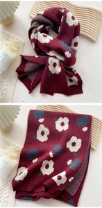 Detail of burgundy knitted scarf featuring large floral jacquard patterns and ribbed edges