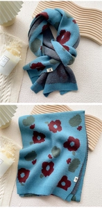 Detail of blue knitted scarf featuring floral patterns and a small stitched H label