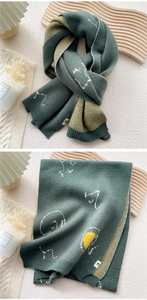 Close-up of knit scarf featuring green animal jacquard pattern and ribbed hem details