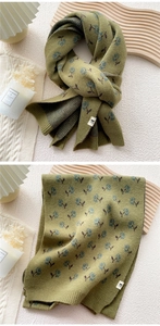 Detail of olive green knit scarf featuring blue floral pattern and woven brand label