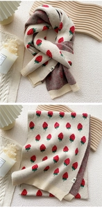 Detailed close-up of knit scarf texture with red strawberry patterns and woven label