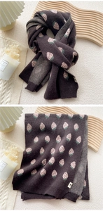 Detail view of thick knitted brown scarf with pink strawberry jacquard pattern and logo patch