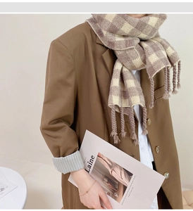 Détail des longs glands tressés sur cette écharpe à carreaux marron et beige chaud