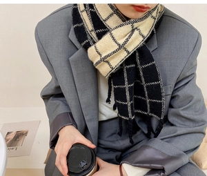 Gros plan d'une écharpe à carreaux noirs et blancs avec franges portée sur un blazer gris