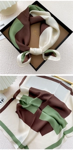 Detail of a silk scarf with geometric blocks in green and brown inside a gift box