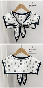 Detail of white scarf shawl with black H-letter print and elegant bow tie-up