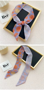 Detail of a slim purple scarf with citrus fruit prints on a gold-framed display board