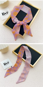 Detail of a purple narrow silk scarf with orange slice prints tied in a bow on a display