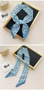 Detail of light blue geometric silk scarf with navy trim tied on elegant stand