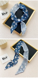 Detail of blue floral skinny scarf with white flower patterns on textured background