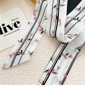 Détail d'un foulard étroit en soie avec rayures noires et motif floral rose