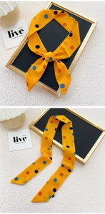 Détail d'un foulard en soie jaune à pois, noué en nœud et suspendu sur un support chic