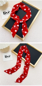 Détail d'un foulard en soie rouge à pois blancs noué en ruban sur un cadre noir
