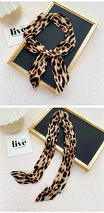 Vue détaillée d'un foulard twilly léopard noué en ruban sur un fond blanc texturé chic