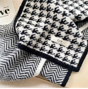 Detailed knit texture of houndstooth scarf with logo label on a soft beige backdrop