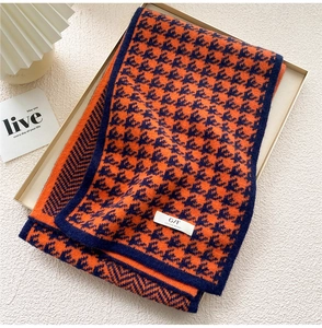 Detail of knitted plaid scarf in orange and navy with a woven logo tag on metal tray