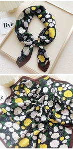 Detailed macro view of black silk scarf with yellow floral print and dark brown rolled edges