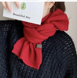 Close-up of red ribbed knit scarf with KEVIN M brand label on black sweater texture