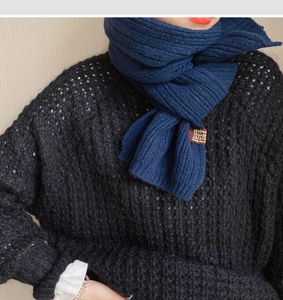Detail of navy blue knitted scarf with vertical ribs and brown leather label texture