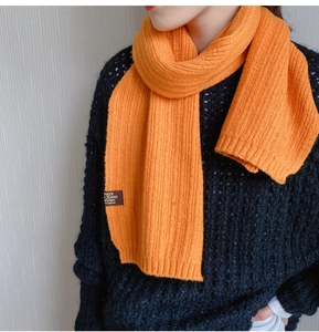 Detail of bright orange ribbed knit scarf with woven label on a black sweater