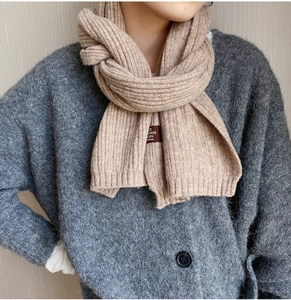 Close-up of beige ribbed knit scarf with leather patch over a grey cardigan sweater