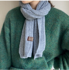 Close-up of gray knit scarf featuring vertical ribbed texture and a brown leather logo tag