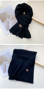 Detail of classic black knit scarf featuring vertical texture and a decorative leather tag