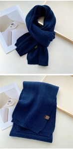 Detail of navy blue ribbed knit scarf with brown square leather label on beige background