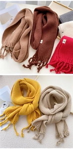 Close-up of thick knitted winter scarves with fringe tassels and woven label in various colors