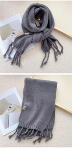 Detailed knit texture of dark grey winter scarf featuring fringe tassels and woven label