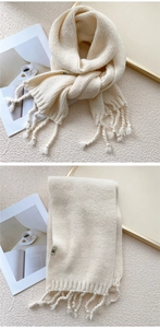 Close-up of thick knit beige scarf with soft tassels and minimalist woven brand label