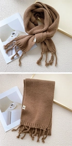 Detailed view of brown knit scarf featuring chunky tassels and a white logo label