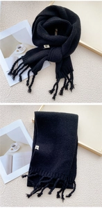Detailed view of black knitted scarf with fringe tassels and small woven label tag