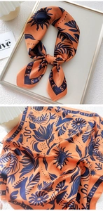 Detailed close-up of orange silk scarf showing sun and palm leaf prints and satin texture