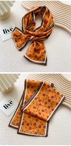 Detail of a thin silk scarf featuring orange floral patterns and striped edge binding
