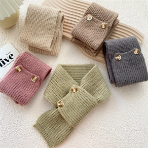 Knitted button cross scarf in five soft colors on a warm wooden decorative tray