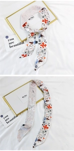 Detail view of a long silk hair scarf featuring black floral prints and orange abstract shapes